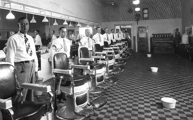 A row of barber chairs in a mid-century barbershop, barbers standing ready