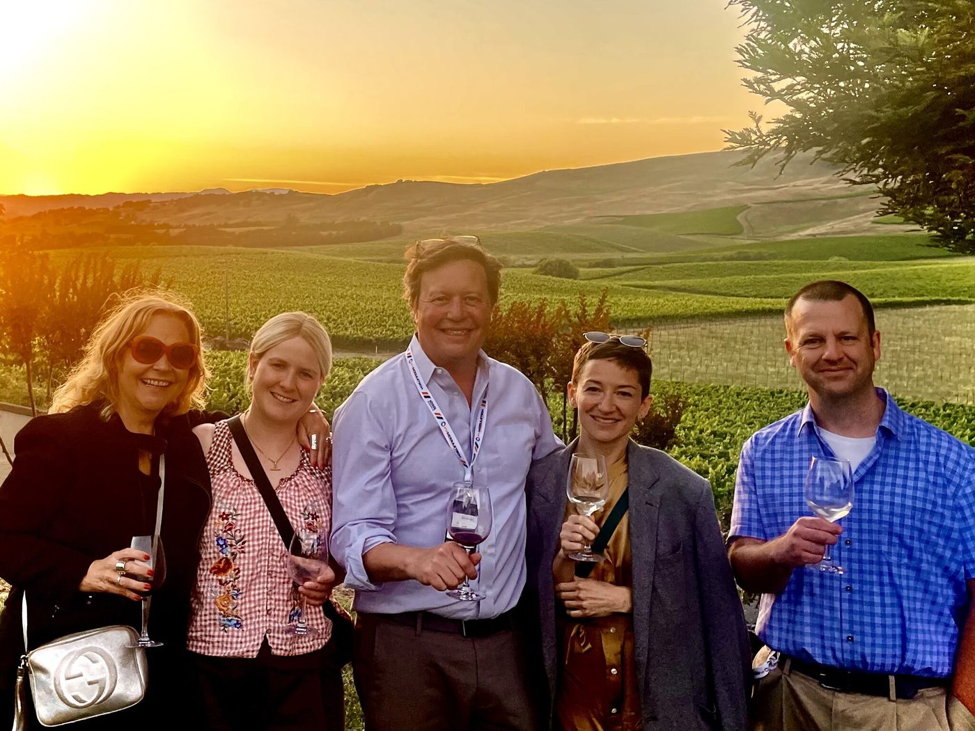 Five PV ModuleTech attendees with wine glasses in front of vineyards at sunset, Sunrise Ranch Winery, Napa