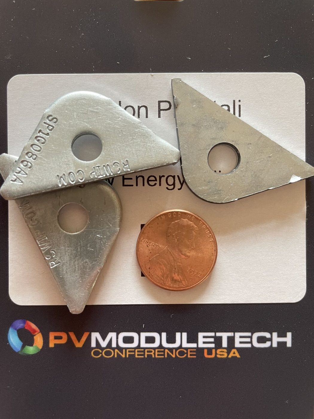 Three StormPlate washers beside a US penny for scale, on a PV ModuleTech Conference USA badge